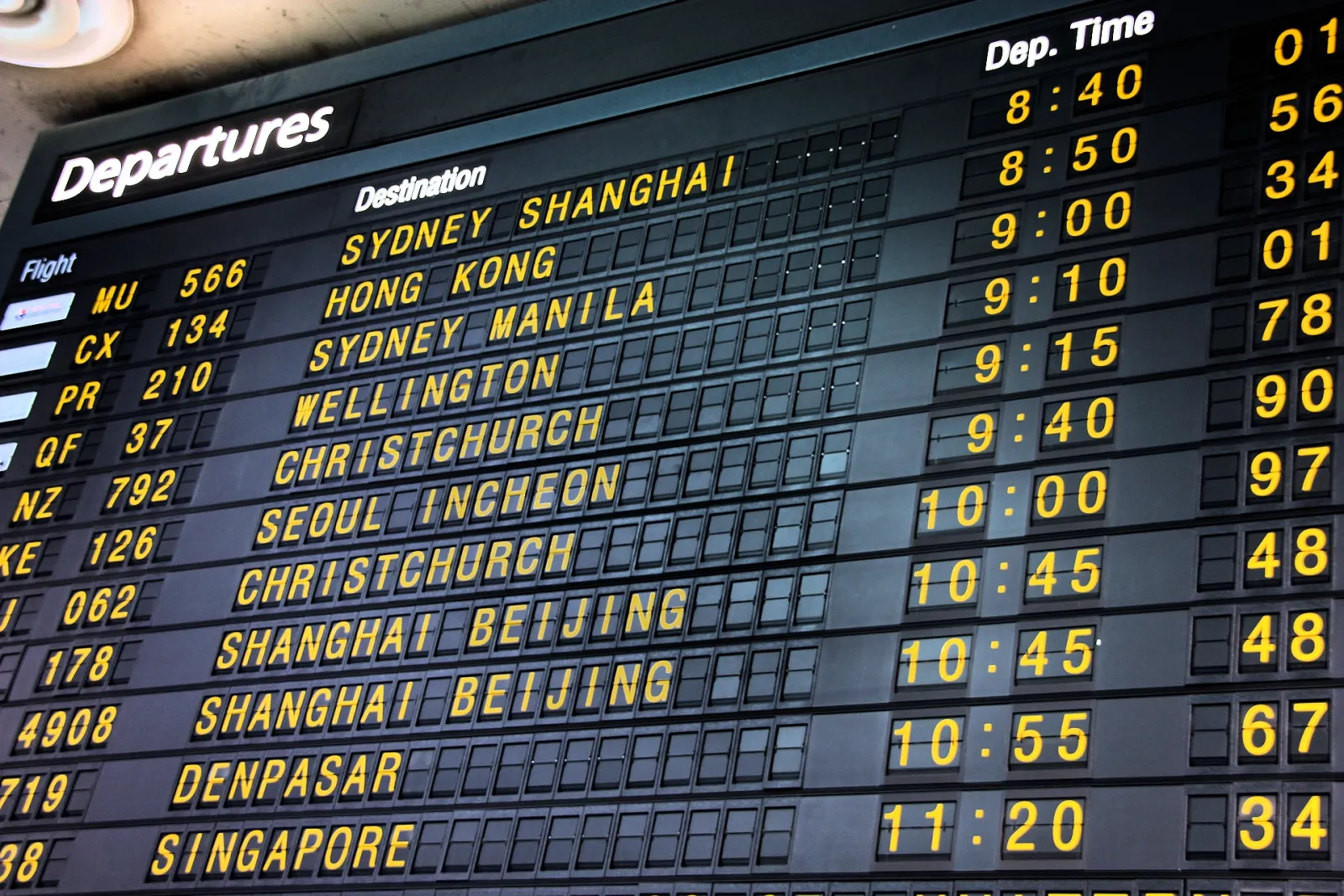 A split-flap departures board listing flights to Sydney, Hong Kong and Singapore